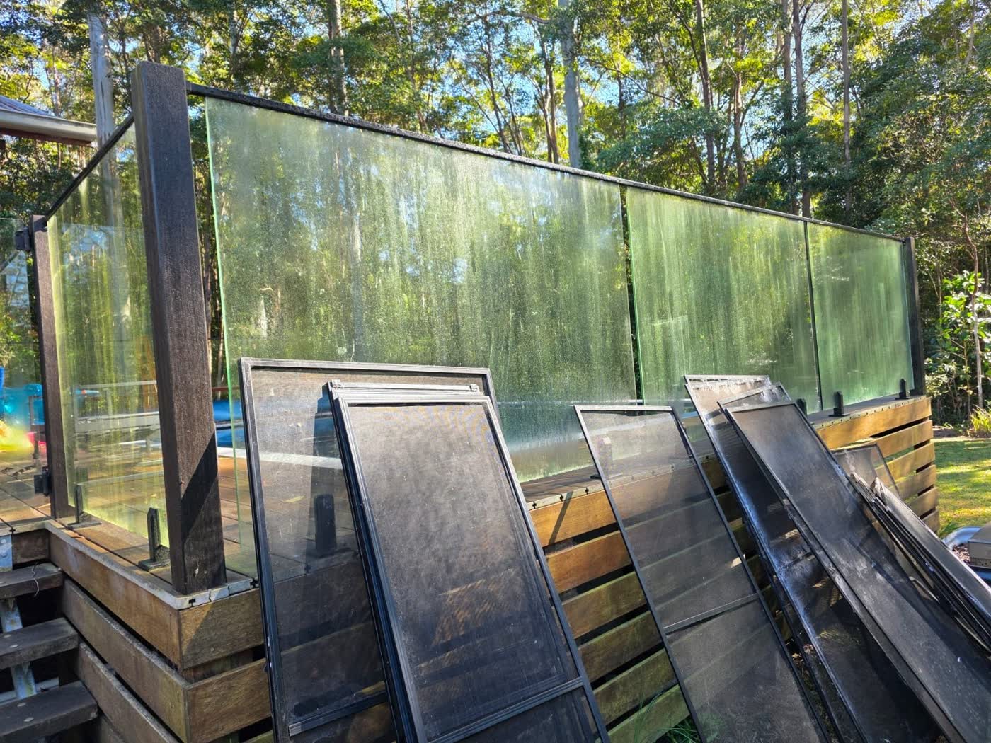 Glass pool fence and timber deck covered in green algae before soft washing